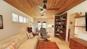 A modern living room with a wooden ceiling, a beige sofa, a wooden coffee table, and a dining area with a chandelier.