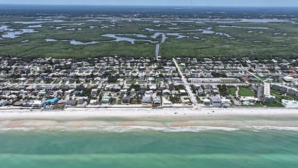 An aerial view of a coastal town with a beach, residential areas, and a large hotel complex.