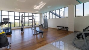 Une salle de sport spacieuse, dotée de divers appareils d’exercice, de grandes fenêtres et d’un plancher en bois.