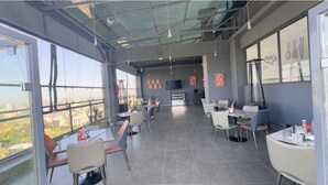 Un espace de restauration moderne, doté de hauts plafonds, de grandes fenêtres et offrant une vue sur la ville.