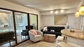 Una sala de estar moderna con sofá, sillón y una mesa de centro. Hay un ventanal corredero que da a un balcón.