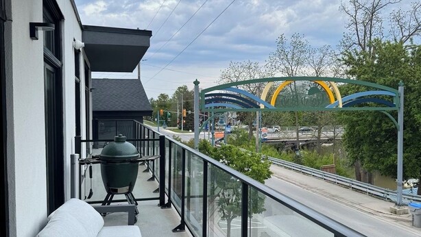 A balcony with a grill, a bench, and a view of a bridge and road.