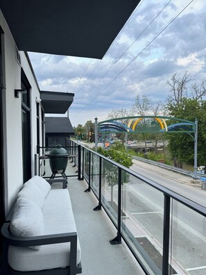 Un balcón con una parrilla, un banco y vistas a un puente y una carretera.