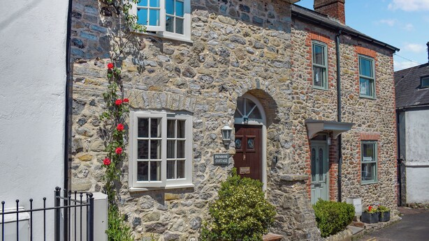 A stone cottage with a white door, a small garden, and a sign reading "Primrose Cottage".