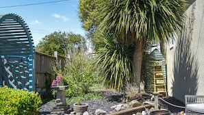 A garden with a wooden deck, a palm tree, and a blue metal gate.