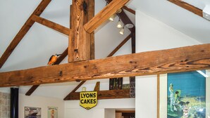 A room with exposed wooden beams, a vintage sign for 'LYONS CAKES', and a framed illustration on the wall.