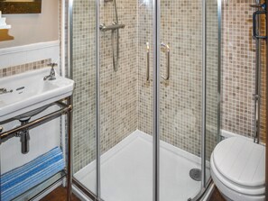 Ein Badezimmer mit einer Glaskabine zur Dusche, einem weißen Waschbecken und einer Toilette.