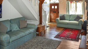 A spacious living area with a staircase, two sofas, a wooden floor, and a red rug.