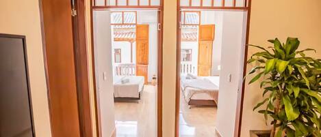 A hallway with a wooden door leading to a bedroom with a bed and a nightstand. There is a potted plant on the right side of the hallway.