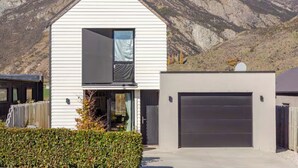 Una casa moderna a due piani con un garage, un balcone e uno sfondo montuoso.