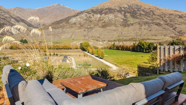 Un patio con tavolo di legno e sedute imbottite, affacciato su un prato e montagne.