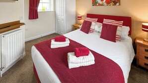 A neatly made bed with red and white bedding, a red headboard, and a painting of flowers on the wall.