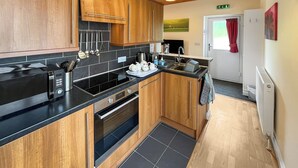 A modern kitchen with wooden cabinets, a black countertop, stainless steel appliances, and a tiled floor.