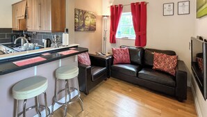 A compact living space with a kitchenette, a sofa with patterned cushions, and a dining area with stools.