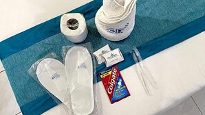 A blue towel, a roll of toilet paper, a pair of slippers, a Colgate toothpaste tube, and a small white box with blue text.