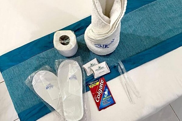 A blue towel, a roll of toilet paper, a pair of slippers, a Colgate toothpaste tube, and a small white box with blue text. - Riverview Resort and Conference Center (Calamba)