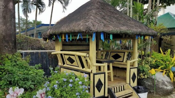 A thatched-roof structure with a wooden bench and steps, surrounded by greenery and flowers.