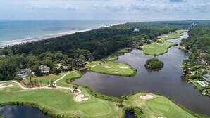Eine Vogelperspektive auf einen Golfplatz mit mehreren Wasserrisiken, einer Brücke und einem Strand im Hintergrund.