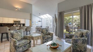 Ein modernes Wohnzimmer mit einem Glastisch, floralen Sofas und einem Essbereich mit Stühlen.