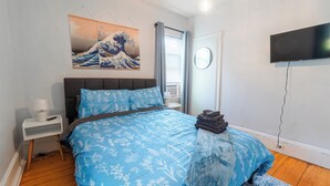 A bedroom with a bed, a TV, a painting, and a window.