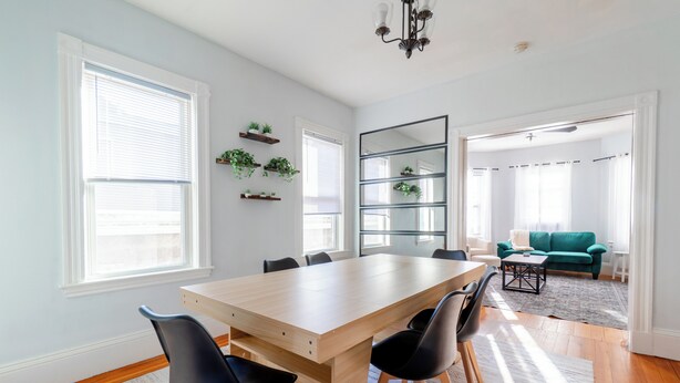 A spacious dining area with a wooden table and black chairs, flanked by large windows and a mirror.