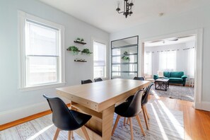 A spacious dining area with a wooden table and black chairs, flanked by large windows and a mirror. - Cozy Davis SQ 4BDs/Free Parking/7 Min to Harvard & MIT/5 Min Walk-Train Station (Somerville)