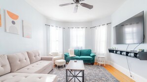 A modern living room with a beige sofa, a teal sofa, a coffee table, and a ceiling fan.