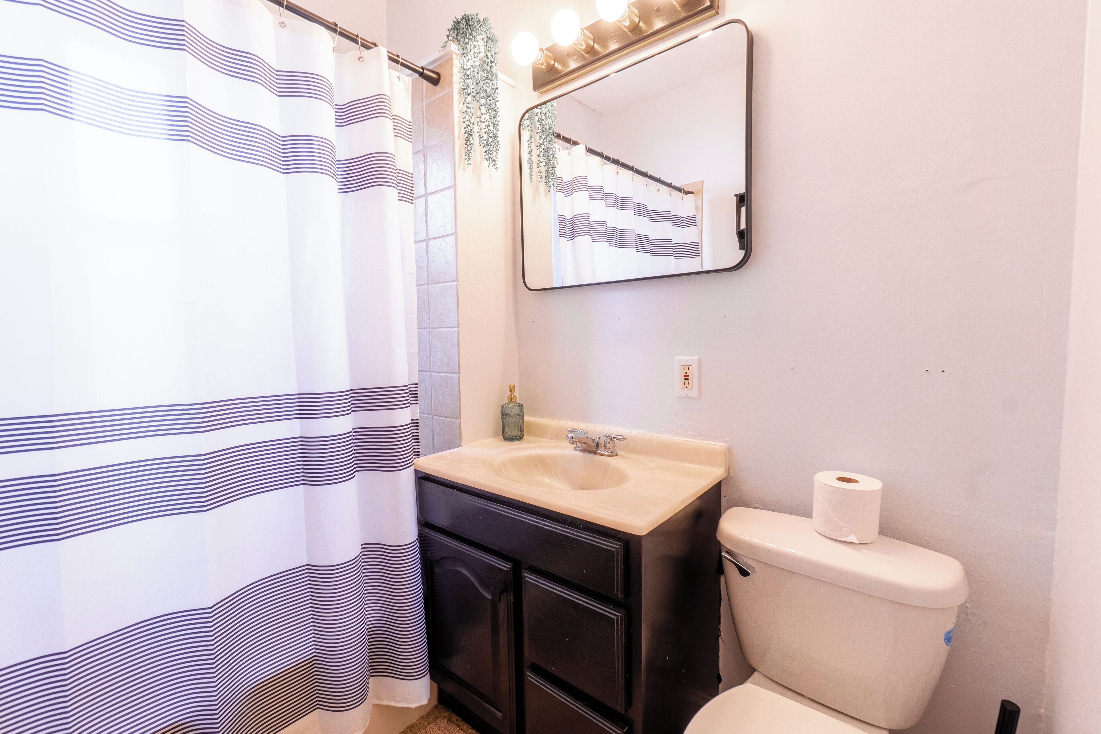 A bathroom with a striped shower curtain, a sink with a mirror above it, and a toilet.