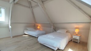 A cozy attic bedroom with two beds, wooden floors, and a sloped ceiling.