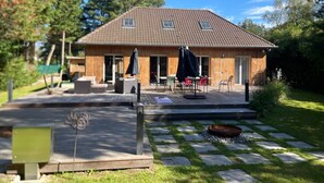 A wooden house with a tiled roof, a patio with outdoor furniture, and a stone pathway leading to the entrance.
