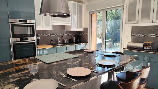 A modern kitchen with a central island, built-in ovens, and a large window.