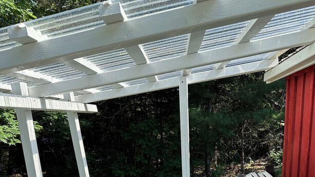 Een hottub met een houten buitenkant, omringd door een houten terras en een witte pergola.