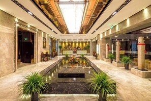 Relax in the serene lobby, surrounded by seating areas and lush greenery, with a central water feature creating a soothing ambiance.