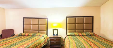Una habitación de hotel con dos camas, una mesita de noche, una lámpara y una silla.