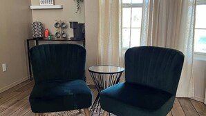 Un salon avec deux fauteuils vert foncé, un tapis rond en fibres naturelles, une table basse et une petite table d’appoint sur laquelle se trouvent une machine à café et des tasses.