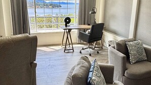 A living room with a view of a lake and mountains, furnished with a sofa, chairs, and a desk. - New! Charming Blue Haven Cottage with Amazing Lake Pend Oreille Views! (Hope)