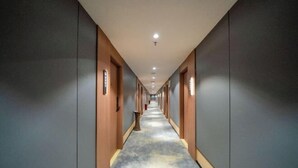 A long, narrow hotel corridor with wooden doors on one side and grey walls on the other. - Bedola Hotel (Xiamen Railway Station Mingfa Plaza) (Xiamen)