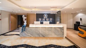 A hotel reception desk with a marble counter, a logo above the counter, and a seating area with a statue. - Bedola Hotel (Xiamen Railway Station Mingfa Plaza) (Xiamen)