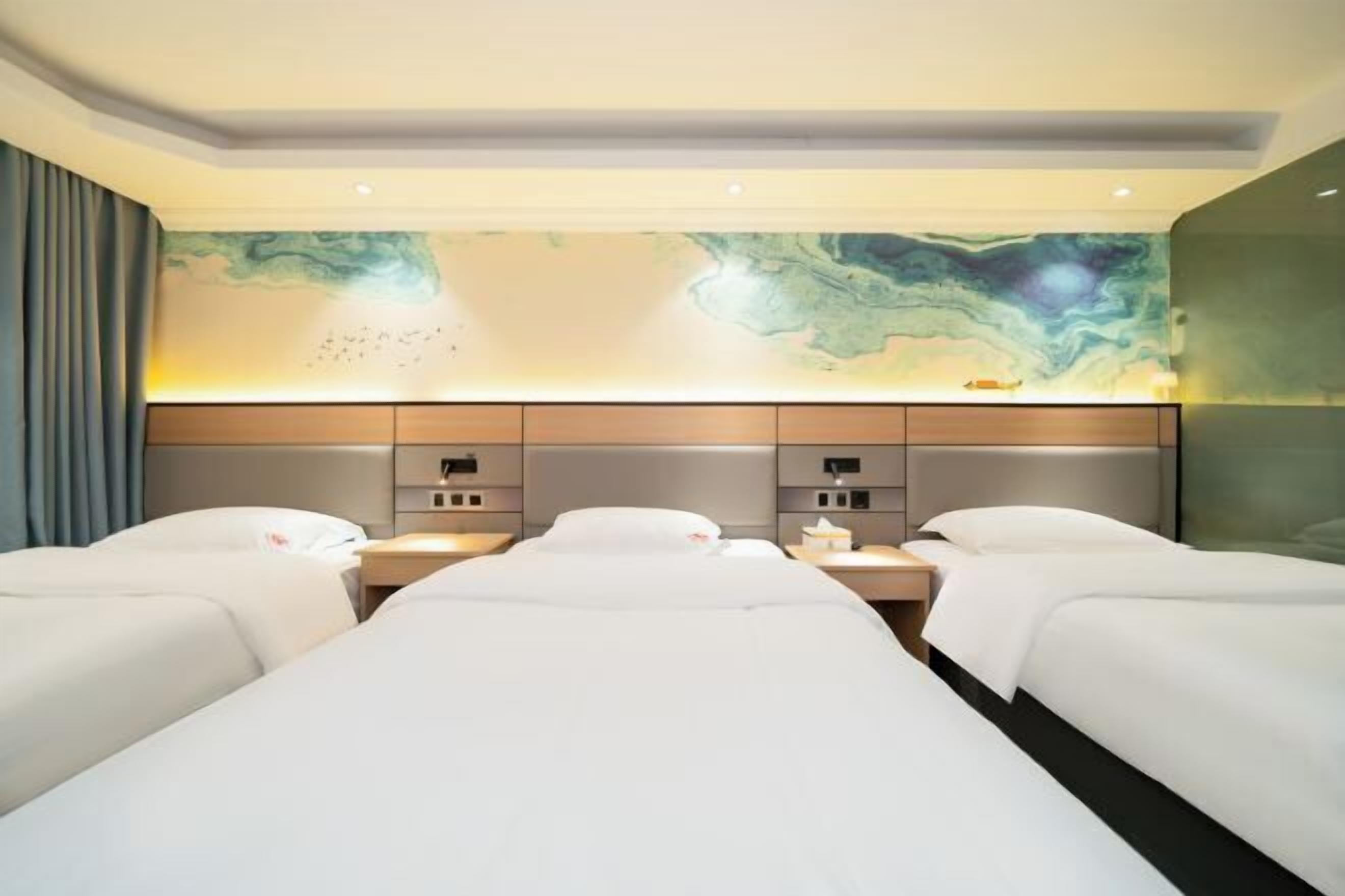 A hotel room with two beds, a marble wall, and a nightstand with a lamp.