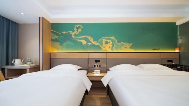 A hotel room with two beds, a large abstract painting on the wall, a small table with a kettle, and a nightstand with a lamp. - Bedola Hotel (Xiamen Railway Station Mingfa Plaza) (Xiamen)