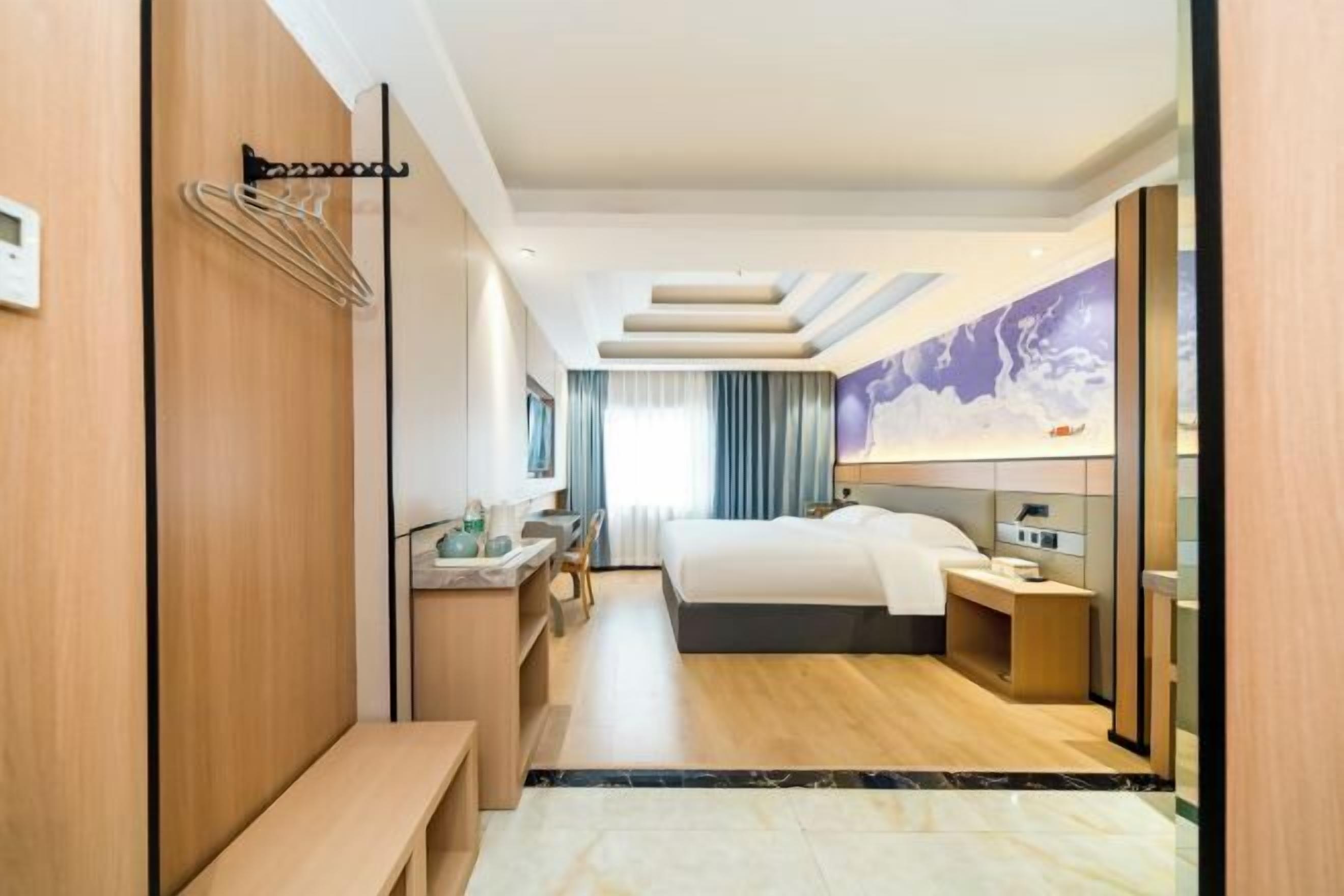 A modern hotel room with a bed, bedside table, desk, and a bathroom with a shower.