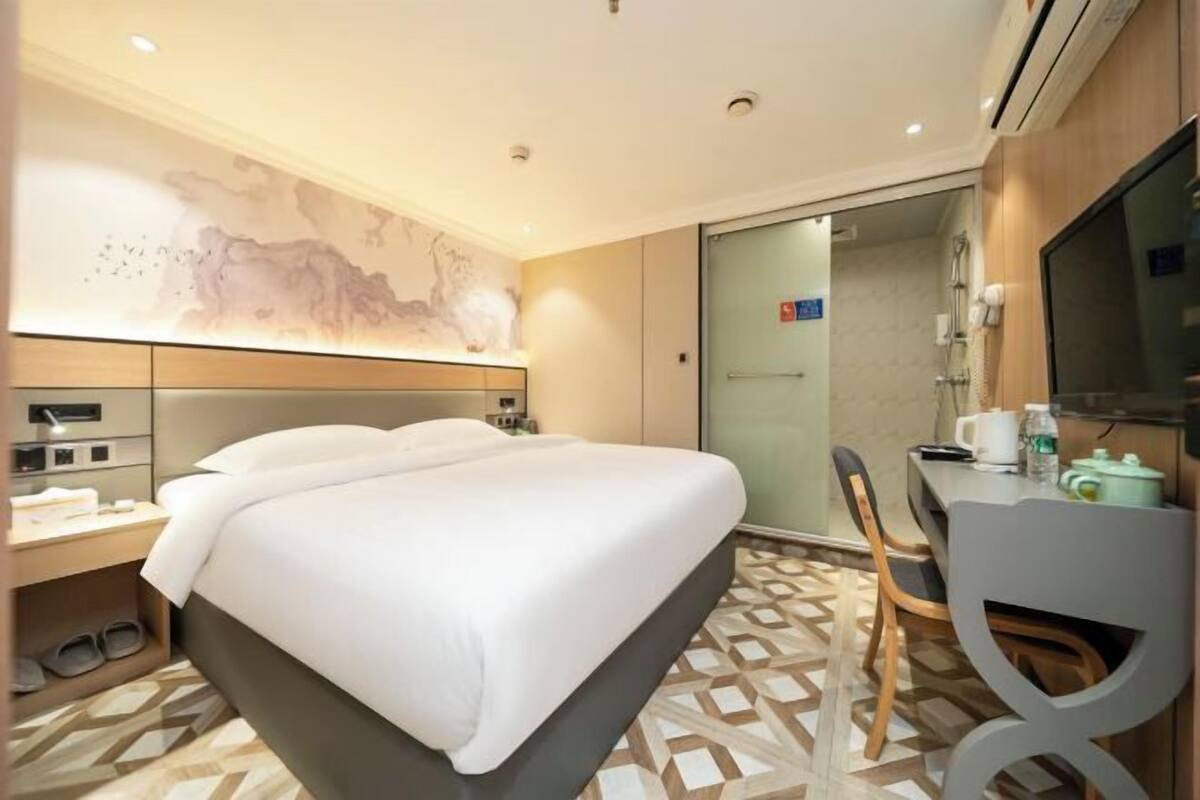 Hotellihuone, jossa on sänky, työpöytä, tuoli, televisio ja suihkutila.