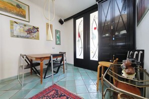 Una habitación con una mesa de comedor, sillas, un tapete estampado, un busto de escultura y un armario negro con puertas de cristal.