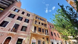 A multi-story building with balconies, a visible storefront with 'ROSA' signage, and a clear blue sky.