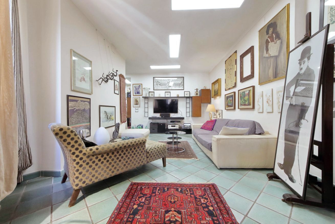 Una sala de estar con un sofá, un sillón estampado, un televisor y varias obras de arte enmarcadas en las paredes.
