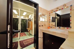Un baño con pared de azulejos, un lavabo, un espejo y una puerta que da a otra habitación.