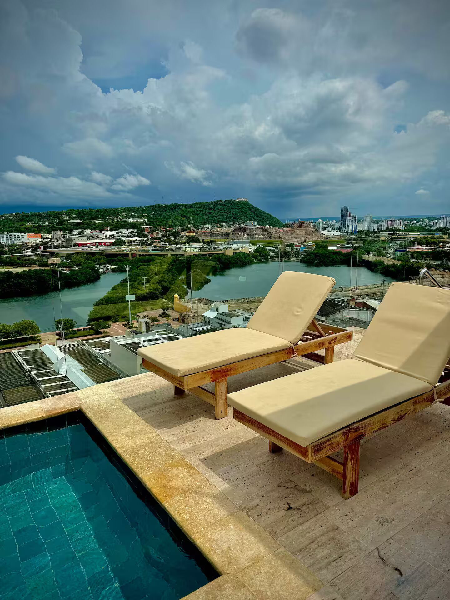 Área da piscina com duas espreguiçadeiras e vista para a cidade e rio.