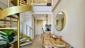 Un interno moderno con una scala a chiocciola, un'area pranzo con mobili in legno e una cucina sullo sfondo.