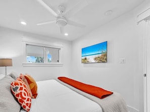 A bedroom with a bed, a ceiling fan, a window, and a beach view painting. - Blue Mountain Beach Villas 5B (Santa Rosa Beach)