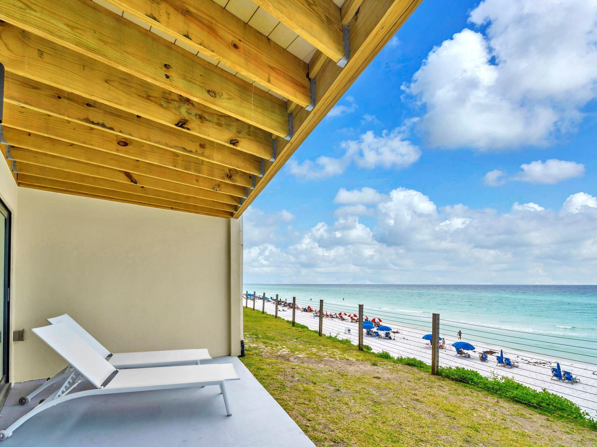 A beach view from a covered patio with a white lounge chair and a wooden ceiling.